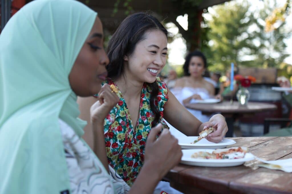 Two women enjoying pizzas at an event catered by A Wandering Fire